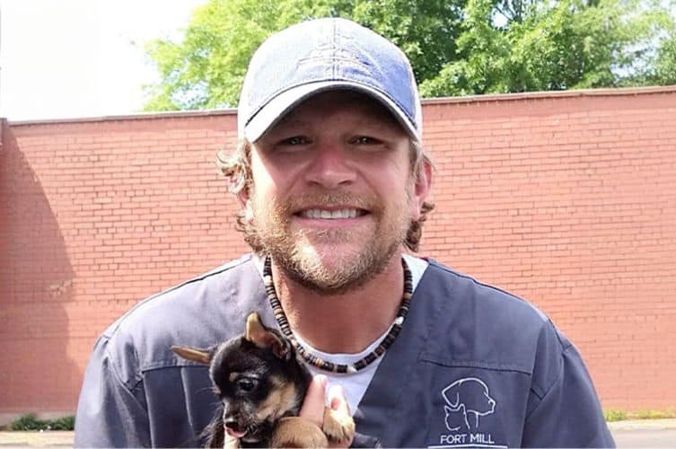 Dr. Ellis, lead veterinarian at Fort Mill Animal Hospital, smiling outdoors while holding a puppy during a sunny day